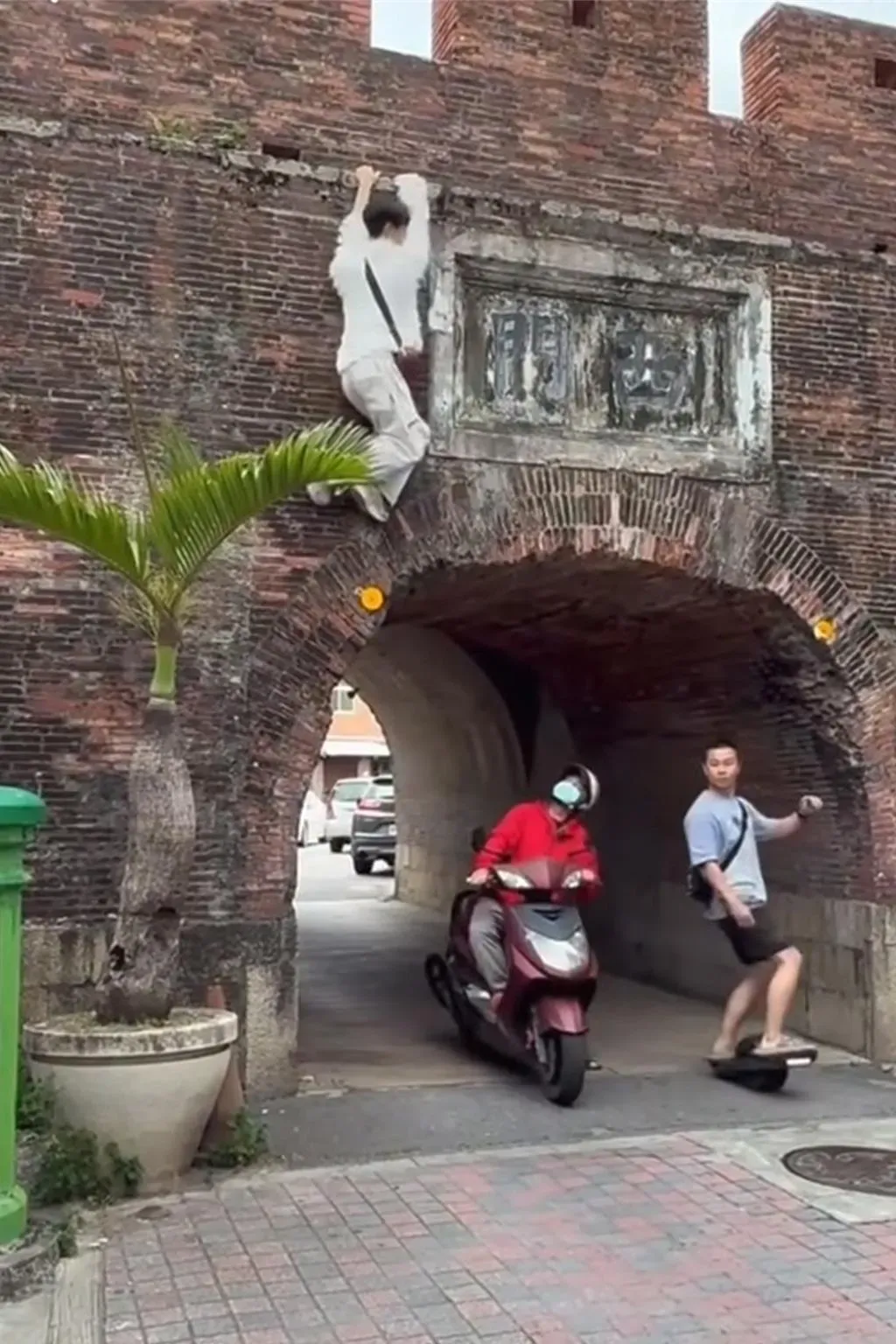 白衣男吊掛在城牆外，底下經過的機車騎士抬頭看白衣男。（圖／翻攝臉書「恆春半島公共事務討論社團」）