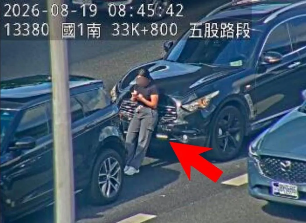 國道1號五股路段今(19)日上午8時許發生追撞事故,後方女駕駛下車後站在兩車之間的「斷腿區」滑手機。(圖/國道1968)