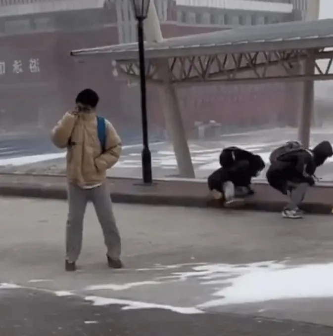 在哈爾濱，有學生在路上冒大風雪前行，有人走不了，用手死命拉住石磚。（圖／星島網）