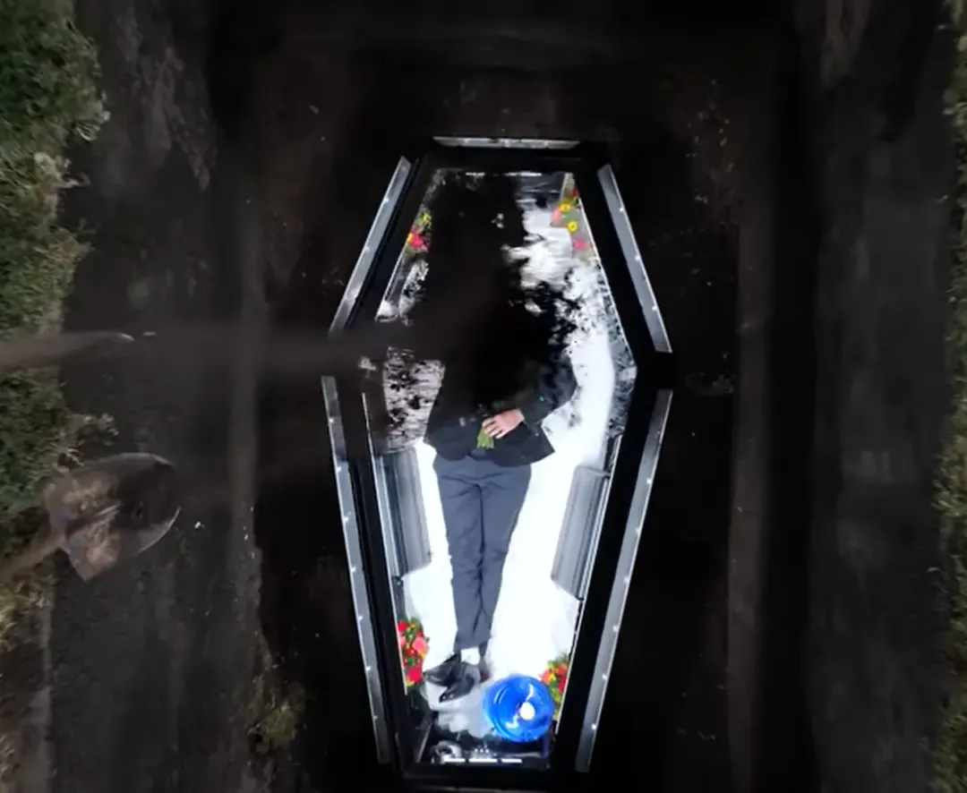 「MrBeast」煞有介事地穿上西裝，將自己和水、糧食關在地底下的透明棺材裡。（圖／翻攝自YouTube@MrBeast）