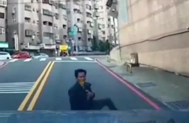 黑衣男坐在地上案著胸口望著車主，被網友質疑「碰瓷」。（圖／翻攝社會事新聞影音）