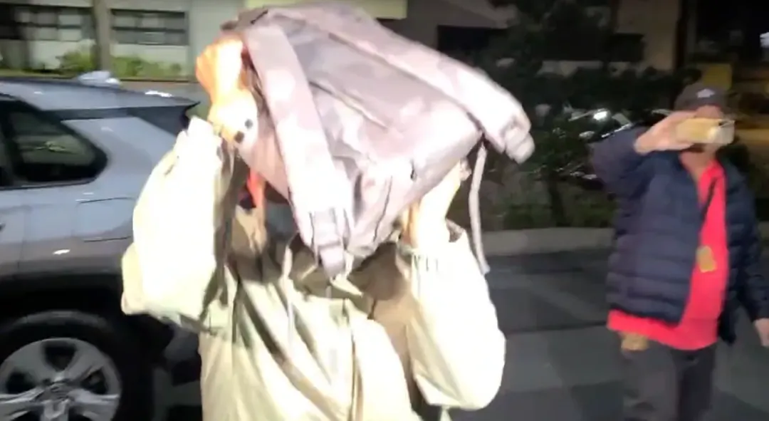 一名被告用書包擋臉躲避媒體追問,差點撞上士檢大門。(圖/中天新聞)