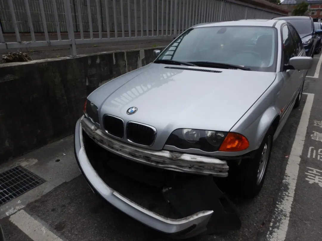 一輛BMW轎車停在路邊遭不明車輛擦撞,保險桿脫落彷彿「落下頦」。(圖/警方提供)