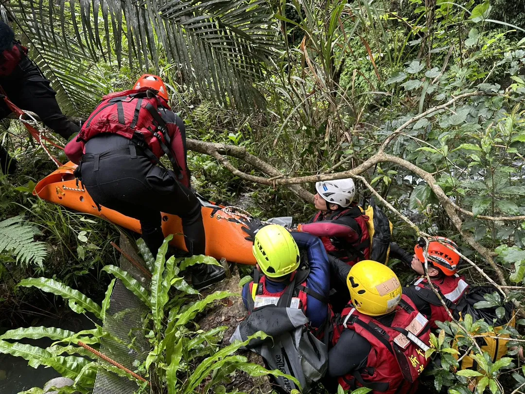 現場地形險峻，救援人員需從產業道路下切溪谷才能接觸到溺者，消防人員運用捲式擔架進行固定，並架設繩索進行拖拉。（圖／消防局提供）