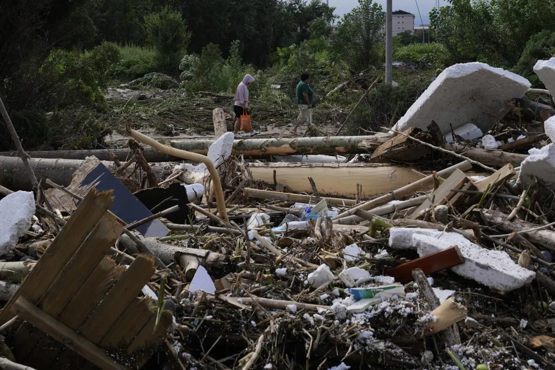 7月28日，暴雨過後，北京密雲居民走在散落著樹枝的受損道路上。（圖／美聯社）