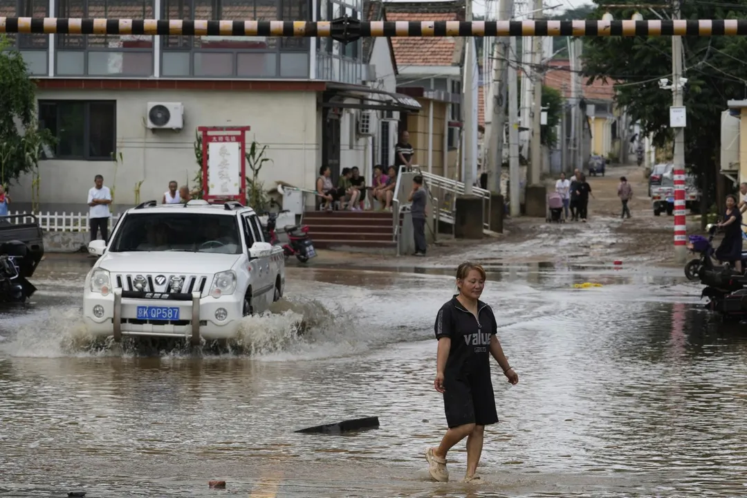 7月28日，北京密雲一名婦女暴雨過後走在淹水的街道。（圖／美聯社）