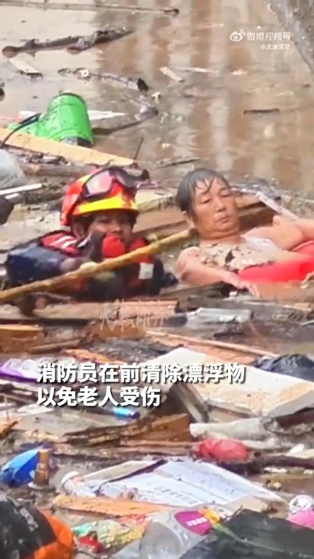 消防員一邊拖老婦前行,一邊撥開漂流物。(圖/翻攝微博「環球網」)