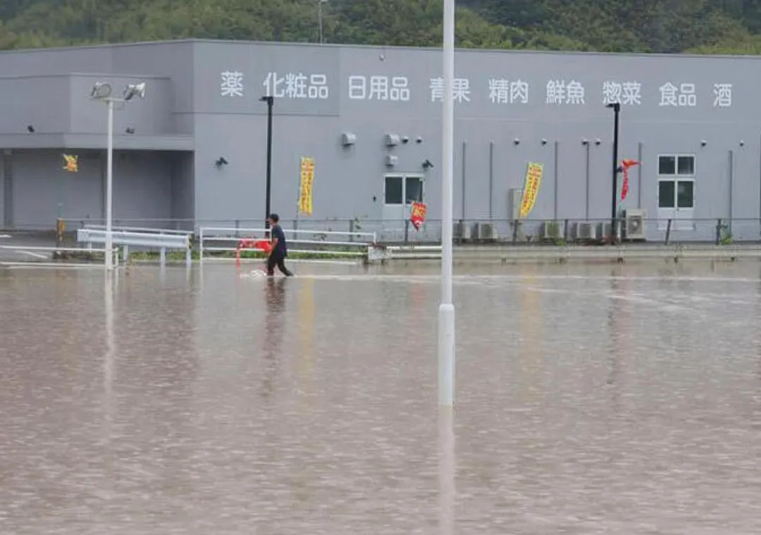 熊本今暴雨成災,一名行人走過被積水的商店停車場。 (圖/美聯社)