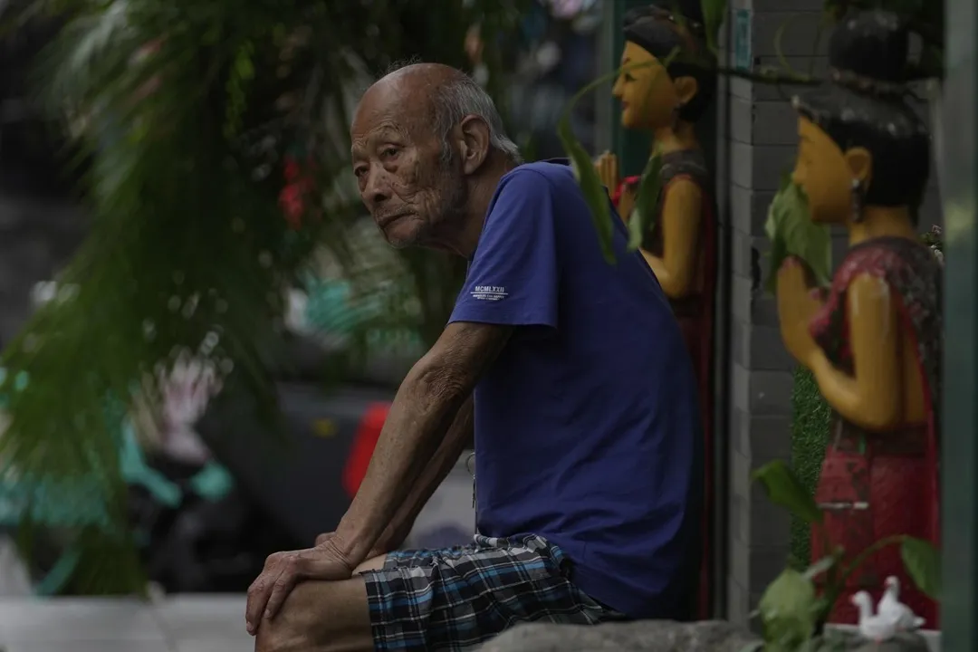 圖為一名長者坐在北京的一家商店外。（圖／美聯社）