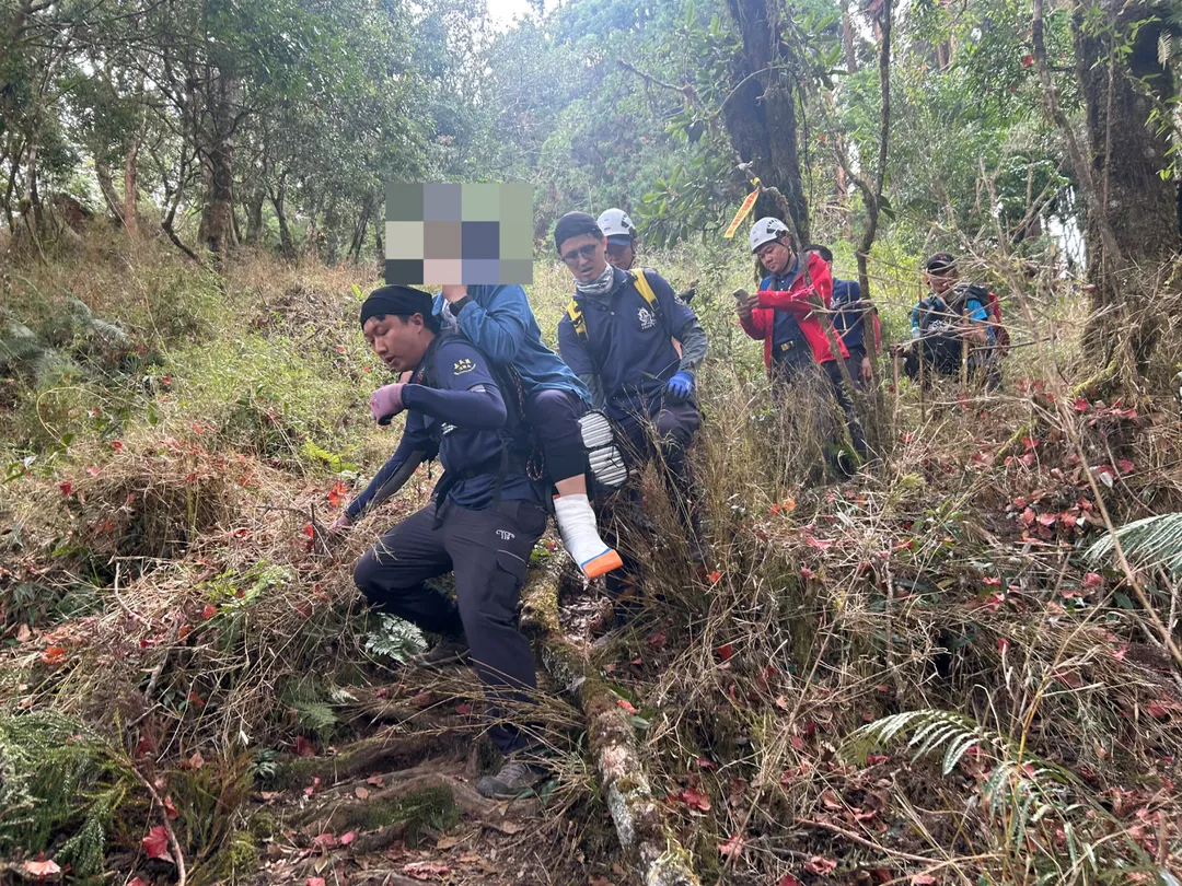 台南市一對夫妻11日至阿里山攀登路況較陡峭的兒玉山路線，妻子摔倒導致左腳踝疑脫臼，嘉義消防人員揹婦人下山。（圖／嘉義縣消防局提供）