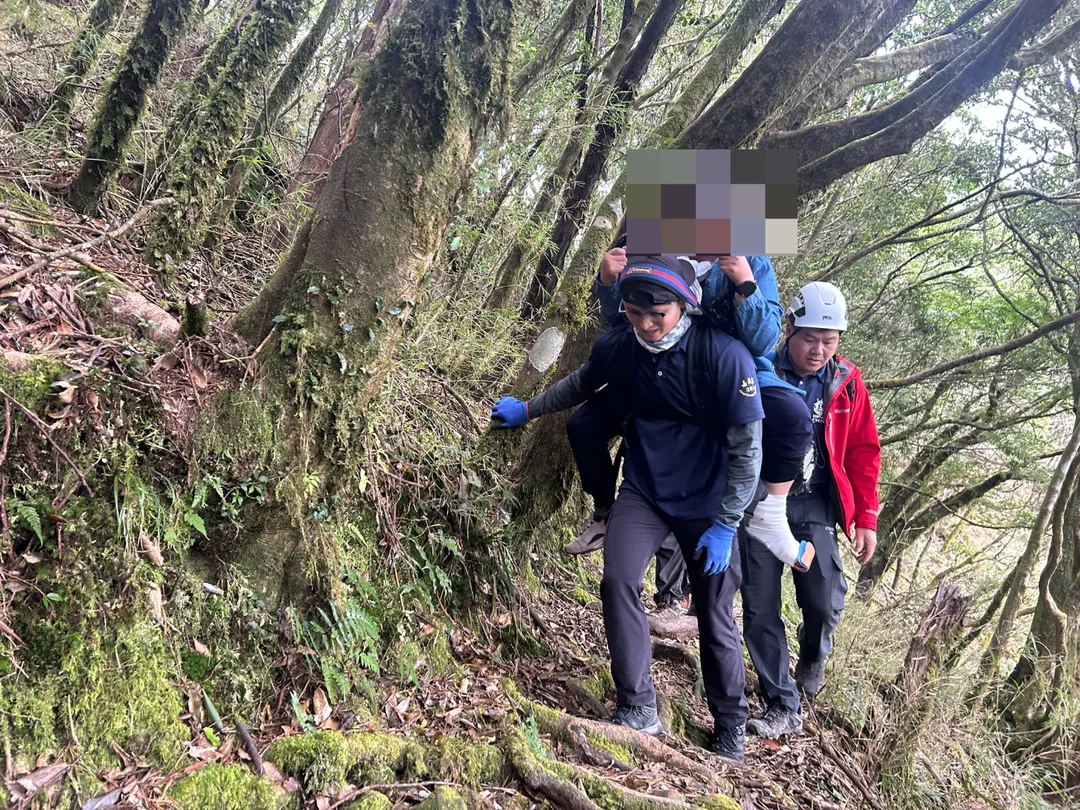 台南市一對夫妻11日至阿里山攀登路況較陡峭的兒玉山路線，妻子摔倒導致左腳踝疑脫臼，嘉義消防人員揹婦人下山。（圖／嘉義縣消防局提供）