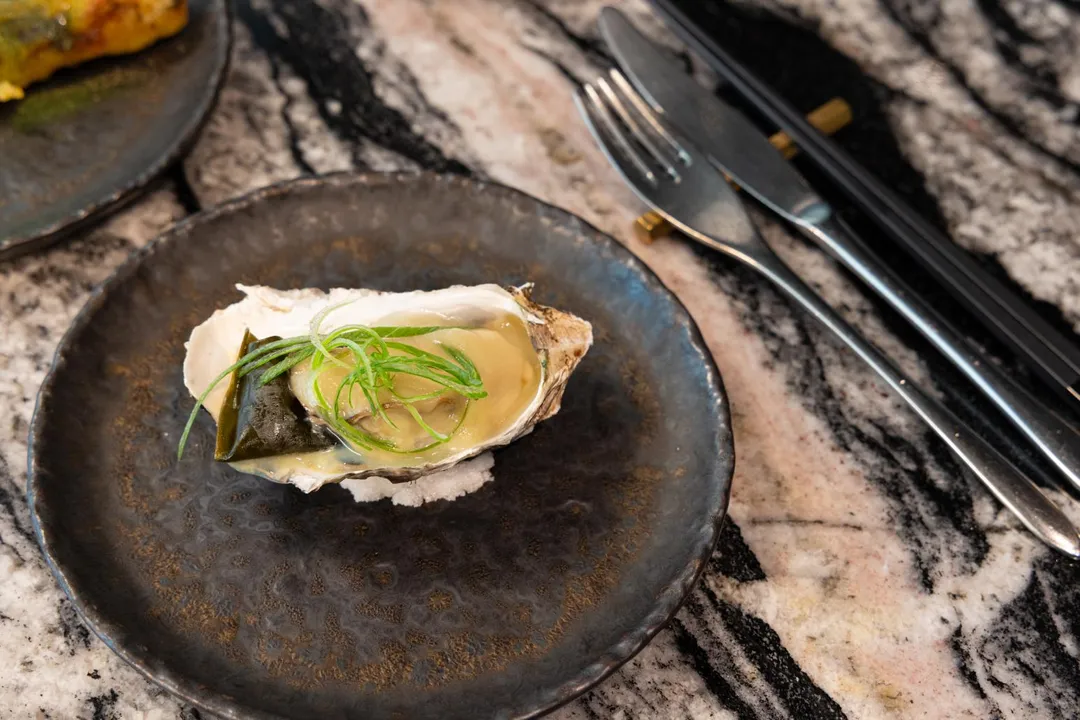 「旨醞」鐵板料理季節新菜〈生蠔佐和玉甜蔥醬〉，以手掌大的帶殼生蠔搭佐昆布，以及由宜蘭三星蔥調製而成的甜蔥醬，讓厚實肥美的生蠔更加水潤鮮甜。（圖／饗賓集團提供）
