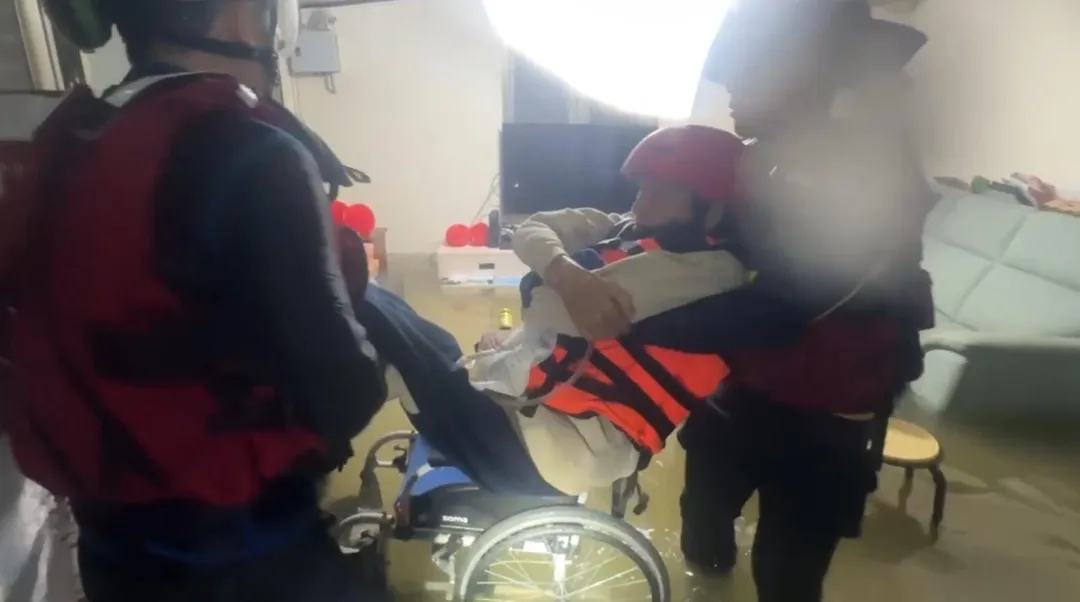 一位民眾行動不便坐在輪椅上，家中已經淹水淹到小腿肚，消防人員將人抬到橡皮艇。（圖／宜蘭縣消防局提供）