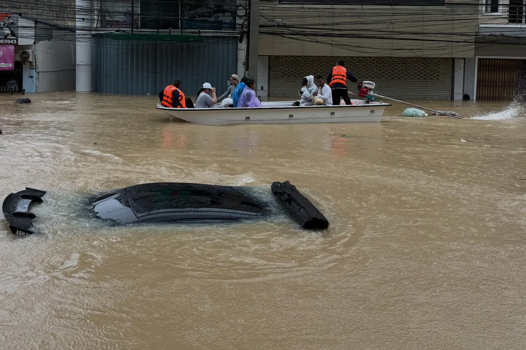 泰政府已將宋卡府全境列為災區,獲救居民乘船艇駛過路面,積水已經淹沒1輛汽車。(圖/美聯社)