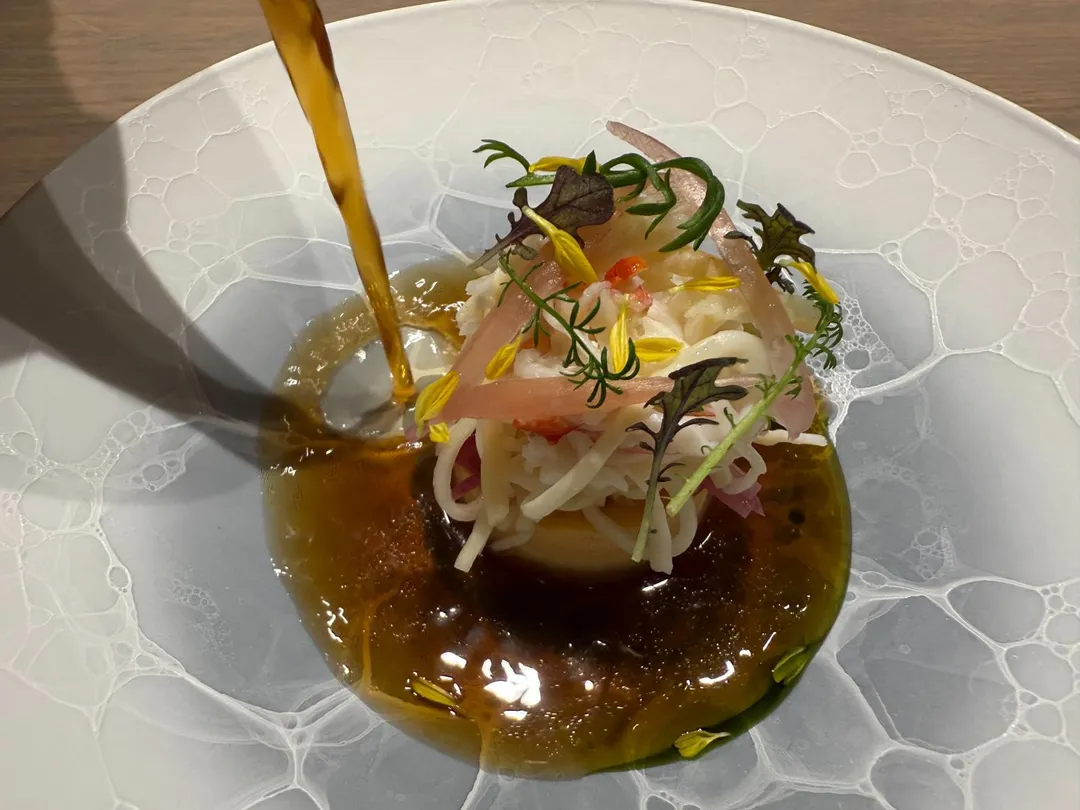 將「料理靈魂」澄清高湯淋上蟹肉團，深琥珀色湯頭口味淡雅。（圖／黃宏輝提供）