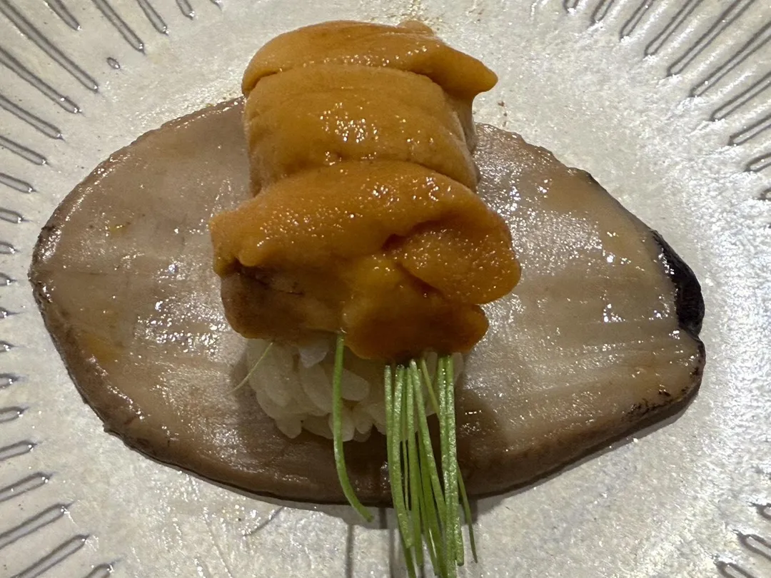 碩大的磯煮南非白鮑切片取代海苔,包裹北海道浜中町產馬糞海膽、京都芽蔥。(圖/黃宏輝提供)
