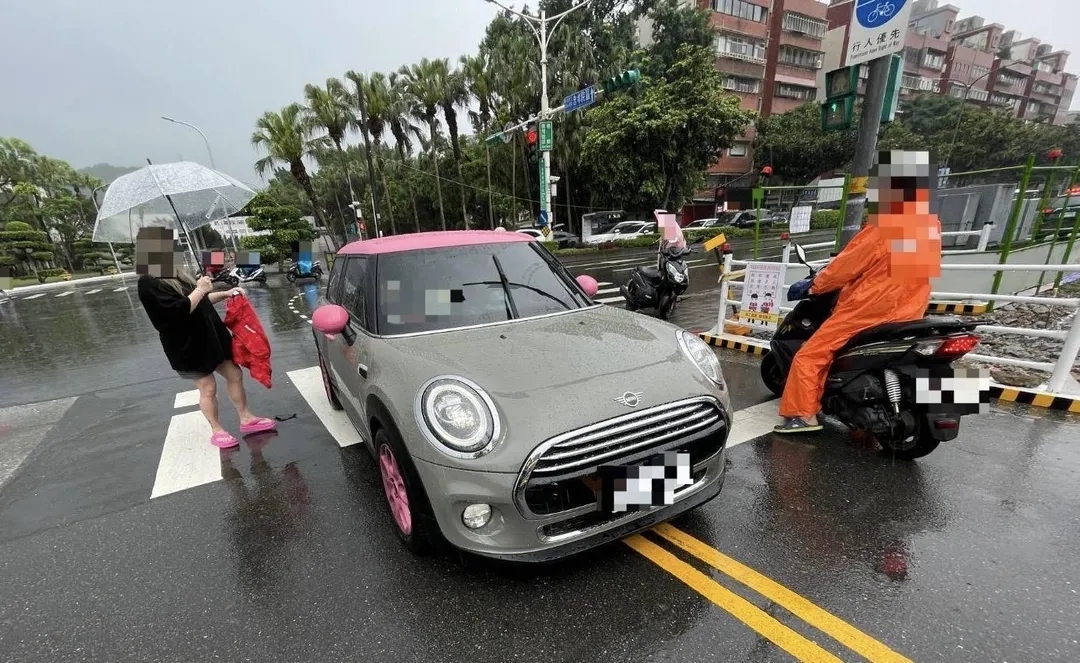 小甜甜駕駛的粉色車頂Mini Cooper車禍現場照，她持傘在路口察看車損。（圖／翻攝畫面）