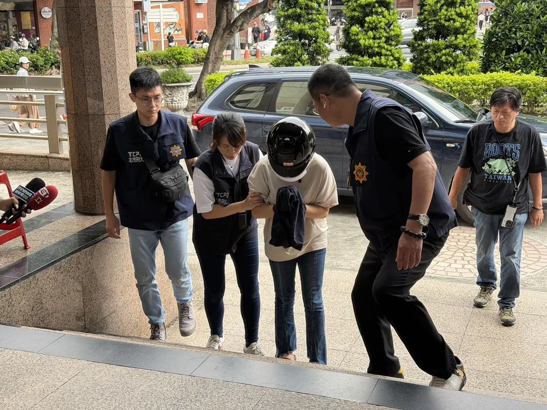 易姓女子今日稍早被戒護帶回分局時，已完全沒有開槍時的狠辣神情。疑似因意識到將面臨嚴苛的法律制裁，她全程低頭發抖、雙手不斷顫抖搓弄，甚至在步行上樓梯時一度腿軟踉蹌、險些跌倒，最後在員警扶持下才得以進入警局。（圖／翻攝畫面）