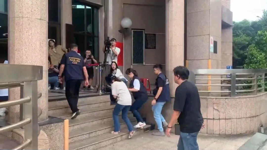 易姓女子今日稍早被戒護帶回分局時，已完全沒有開槍時的狠辣神情。疑似因意識到將面臨嚴苛的法律制裁，她全程低頭發抖、雙手不斷顫抖搓弄，甚至在步行上樓梯時一度腿軟踉蹌、險些跌倒，最後在員警扶持下才得以進入警局。（圖／翻攝畫面）