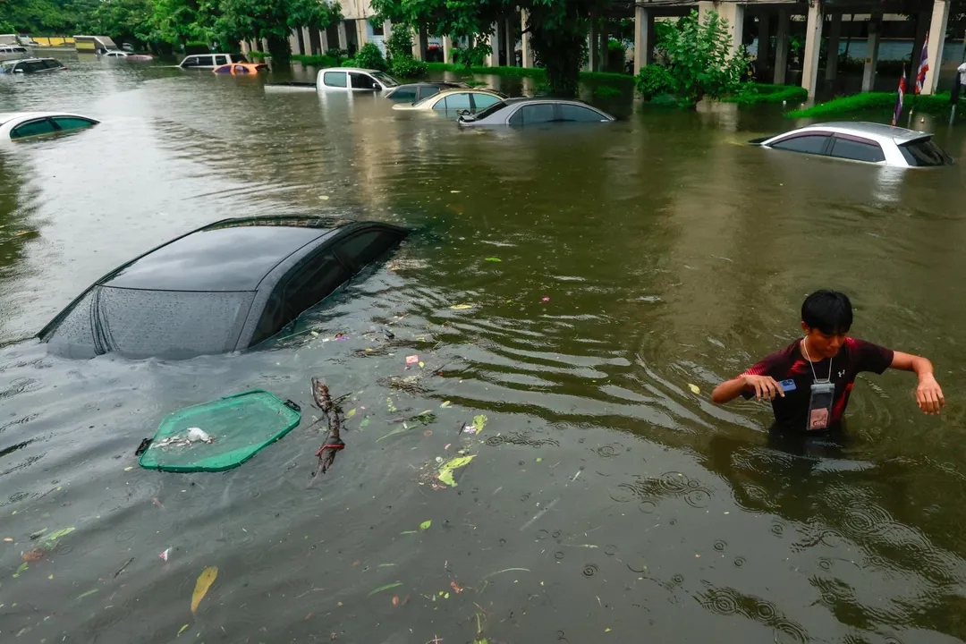一名男子走過水深及胸的積水，一旁汽車已幾乎滅頂。（圖／路透社）