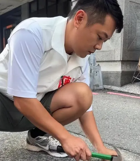 高雄市鳳山區和德里里長參選人陳柏鴻因接獲在地里民反映水溝蓋發出噪音，便自備鐵鎚與金屬墊片，親自將墊片敲入溝蓋縫隙中以減少震動異音。（圖／sw5859）
