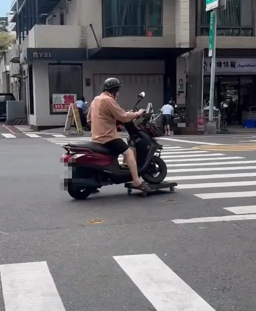 台南市一名騎士疑似因為前輪故障,竟放置在平板車上,用腳在馬路上滑動,非常危險。(圖/翻攝畫面)