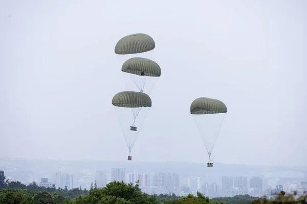 C-130運輸機自高空釋放軍品,透過降落傘緩降至指定空投區,陸軍裝甲542旅官兵迅速進場接收,展現聯合後勤補給效率。(圖/軍聞社)