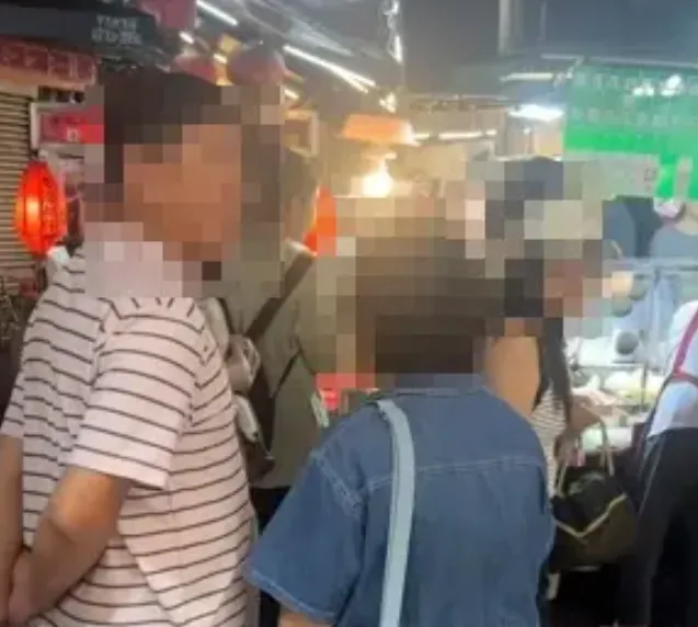 一對男女在等人排隊購買因黃仁勳爆紅的阿婆水果，站在一旁服飾店門口，店家勸導後爆發口角。（圖/翻攝畫面）