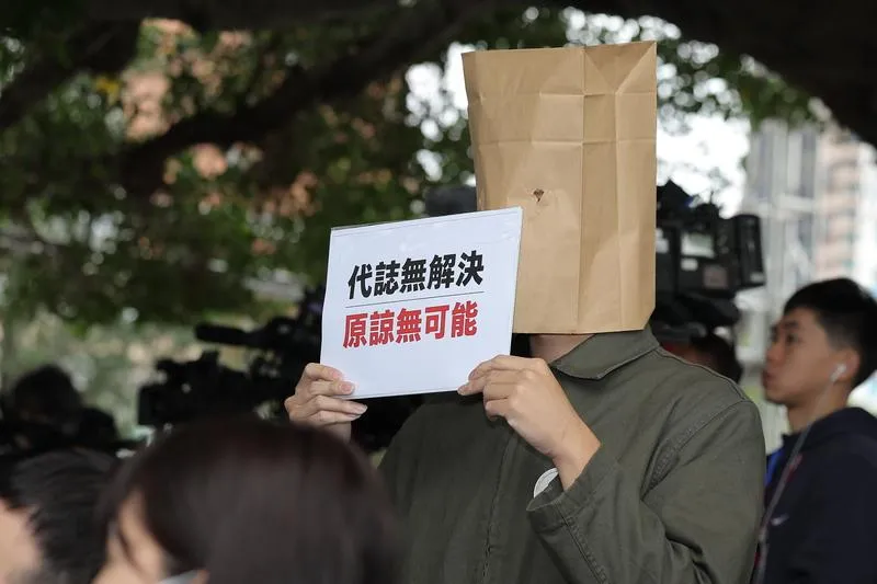 台北市長蔣萬安在228事件紀念會致詞時，現場有受難者家屬頭戴紙袋，並拿著「代誌無解決，原諒無可能」標語。（圖／中央社）