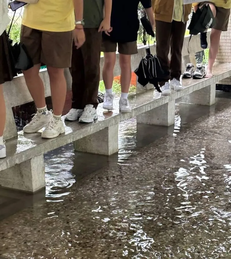 國立羅東高中校園重要通道風雨走廊因暴雨積水達30公分深，學生為了通行被迫脫掉鞋襪赤腳涉水，或改走兩側座椅避開淹水區域。（圖／羅東高中提供）