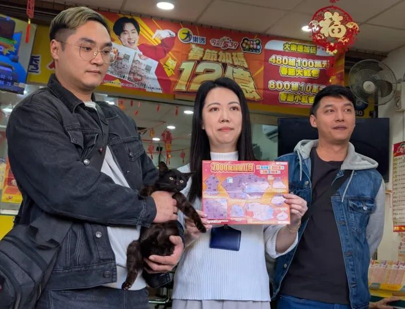 台中陳姓兄弟（左、右）日前認養一隻黑色流浪貓，2人12日帶著黑貓到南區1家彩券行購買刮刮樂，竟刮中新台幣100萬元獎項，13日重回彩券行分享喜悅。（圖／中央社）