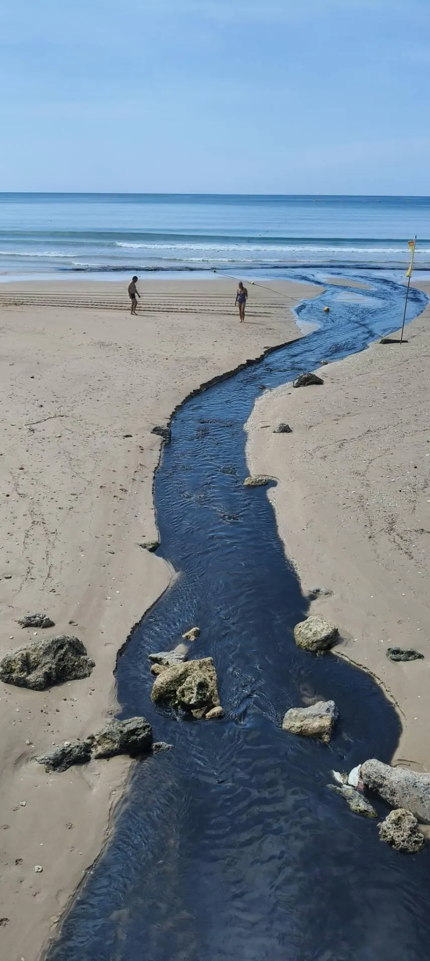 大量深黑色污水經過沙灘上一條黑色溝渠流向大海。（圖／民眾提供）